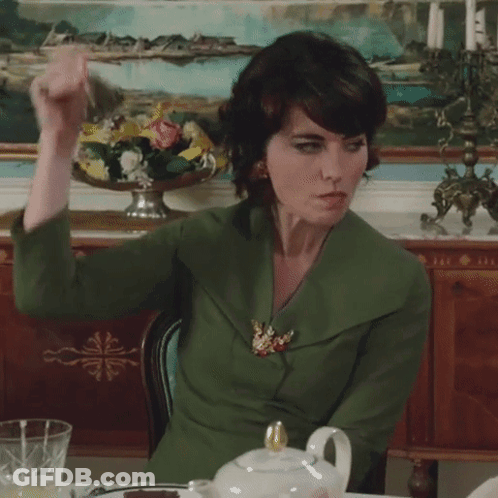 A Woman In A Green Jacket Sits At A Table GIF