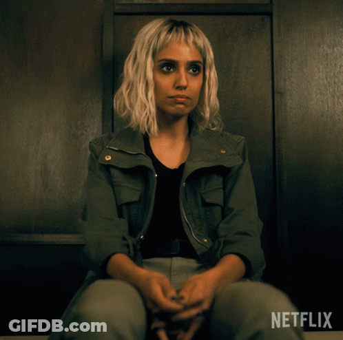 A Woman In A Green Jacket Sits In A Dark Room With Netflix Written On The Bottom GIF