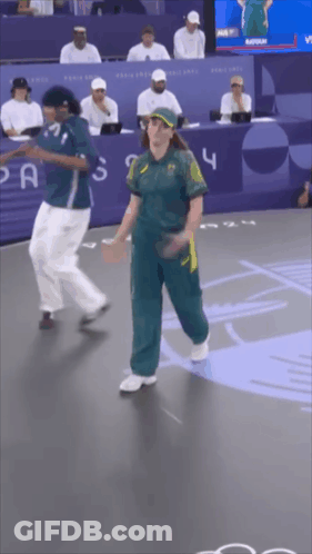 A Woman In A Green Jumpsuit Is Dancing With A Man In A Blue Shirt With The Number 4 On It GIF