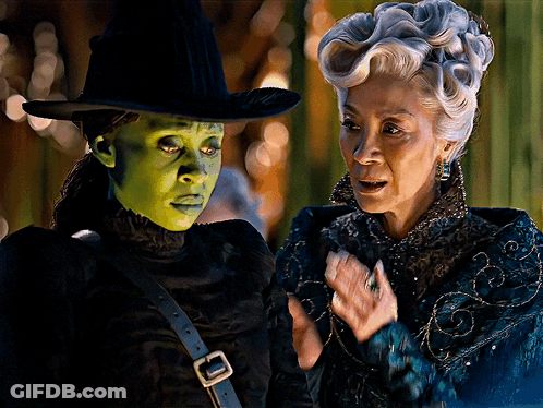 A Woman In A Green Mask Stands Next To Another Woman GIF