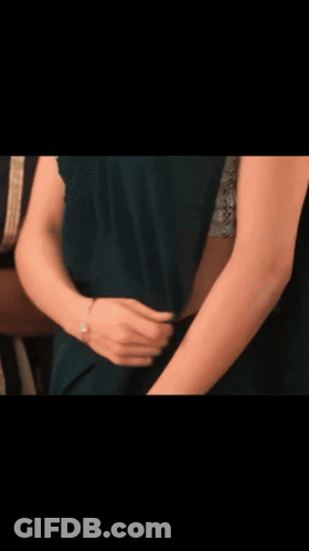 A Woman In A Green Saree Is Standing In Front Of A Red Curtain GIF