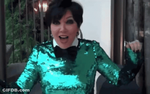 A Woman In A Green Sequined Top And Black Bow Tie Is Sitting On A Couch . GIF