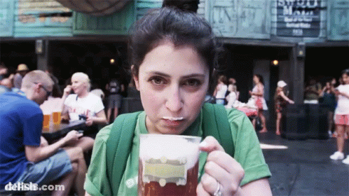 A Woman In A Green Shirt Is Drinking A Beer From A Plastic Cup GIF