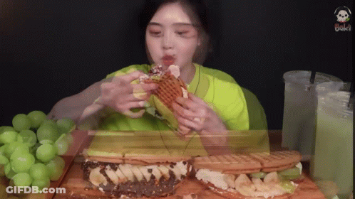 A Woman In A Green Shirt Is Eating A Sandwich With Bananas On It GIF