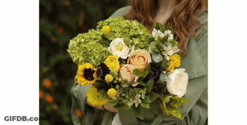 A Woman In A Green Shirt Is Holding A Bouquet Of Flowers . GIF