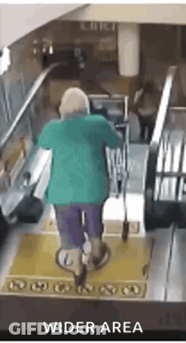 A Woman In A Green Shirt Is Riding An Escalator In A Wider Area GIF