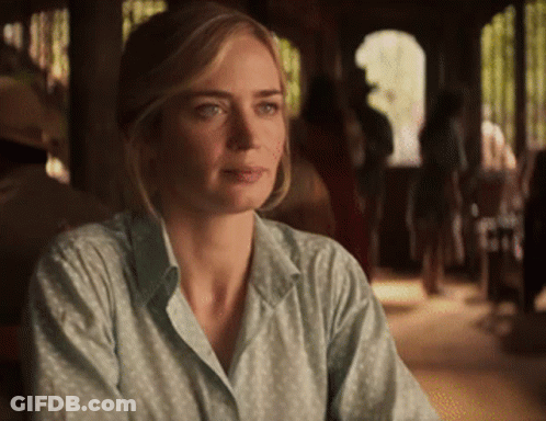 A Woman In A Green Shirt Is Sitting At A Table And Looking At The Camera GIF