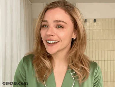 A Woman In A Green Shirt Is Smiling In Front Of A Yellow Tiled Wall GIF