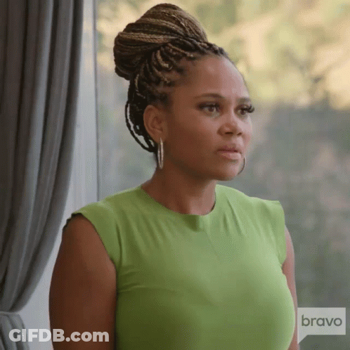 A Woman In A Green Shirt Is Standing In Front Of A Window With A Bravo Logo In The Corner GIF