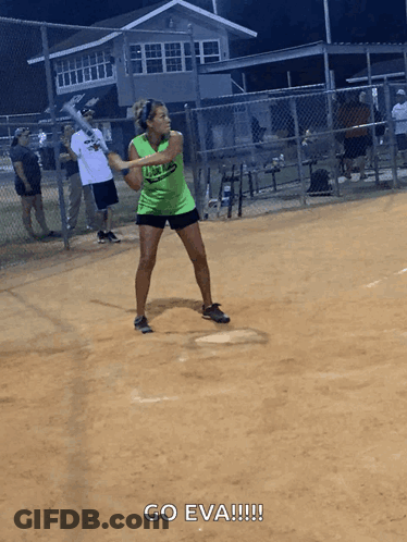 A Woman In A Green Shirt Is Swinging A Bat At A Ball GIF