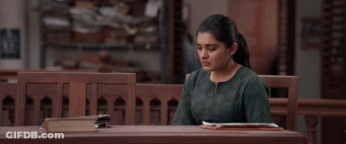 A Woman In A Green Shirt Sits At A Wooden Table GIF