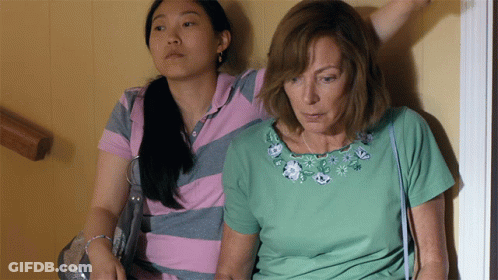 A Woman In A Green Shirt Sits Next To Another Woman In A Pink And Gray Striped Shirt GIF