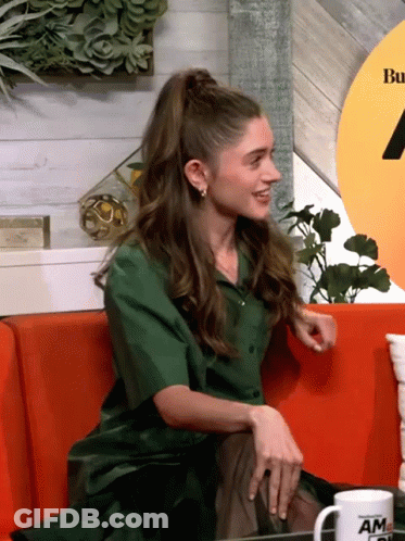 A Woman In A Green Shirt Sits On A Red Couch Next To A Mug That Says Am GIF