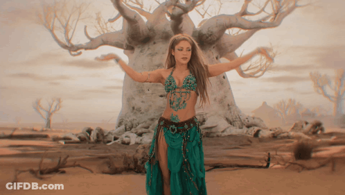 A Woman In A Green Skirt Is Dancing In Front Of A Tree GIF
