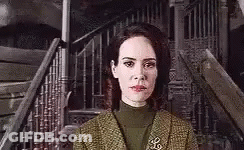 A Woman In A Green Suit Is Standing In Front Of A Staircase . GIF