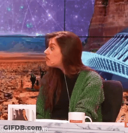 A Woman In A Green Sweater Is Sitting At A Table With A Mug That Says ' Nevada ' On It GIF
