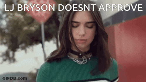 A Woman In A Green Sweater Is Standing In Front Of A Red Sign That Says " Lj Bryson Doesnt Approve " GIF