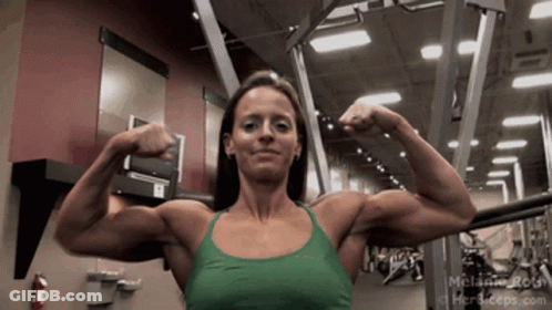 A Woman In A Green Tank Top Is Flexing Her Muscles In A Gym .. GIF