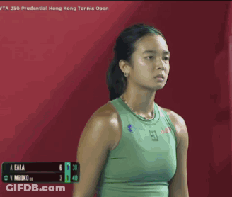 A Woman In A Green Tank Top Is Standing In Front Of A Red Background . GIF