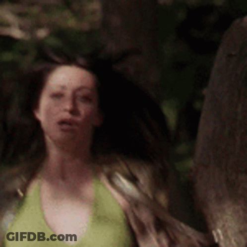 A Woman In A Green Tank Top Is Walking Through A Forest . GIF