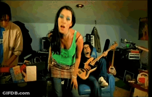 A Woman In A Green Tank Top Stands In Front Of A Man Playing A Guitar GIF