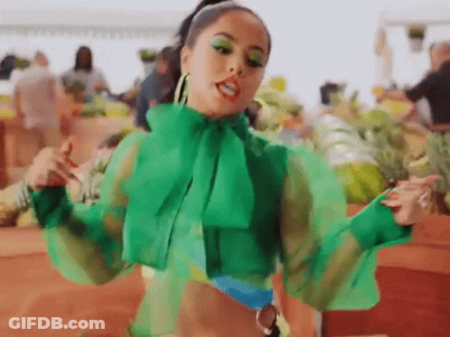 A Woman In A Green Top Is Standing In Front Of A Market . GIF