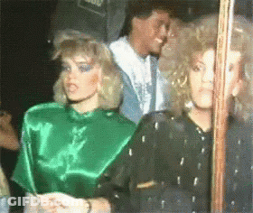 A Woman In A Green Top Is Standing Next To A Woman In A Black Top GIF
