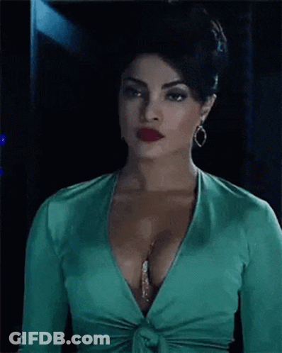 A Woman In A Green Top With A Plunging Neckline And Red Lips Is Standing In A Dark Room . GIF