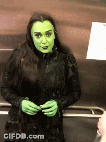 A Woman In A Green Witch Costume Stands In An Elevator GIF
