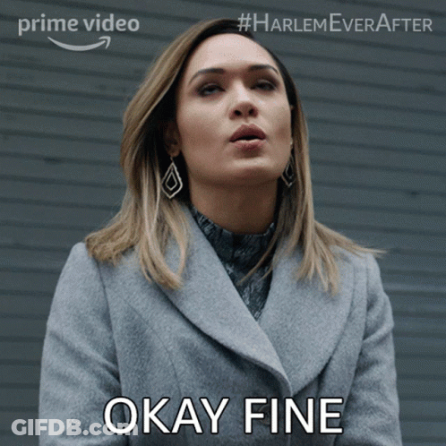 A Woman In A Grey Coat Says Okay Fine In Front Of A Wall GIF