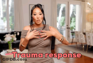 A Woman In A Grey Dress Is Standing In A Living Room With The Words Trauma Response Written Above Her GIF