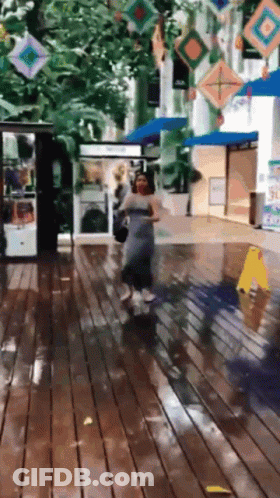 A Woman In A Grey Dress Is Walking On A Wet Floor GIF