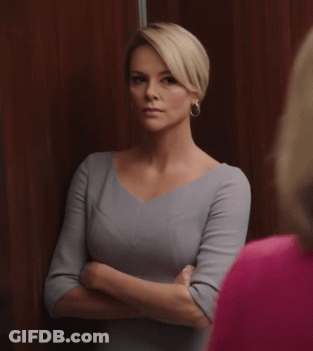 A Woman In A Grey Dress Stands With Her Arms Crossed Looking At Another Woman In A Pink Shirt GIF
