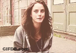 A Woman In A Grey Hoodie Is Sitting On The Sidewalk In Front Of A Building GIF