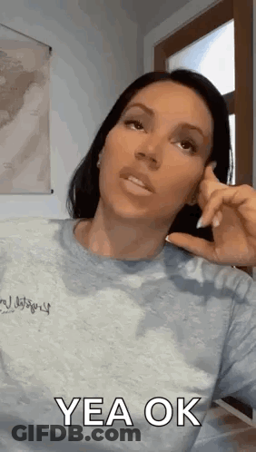 A Woman In A Grey Shirt Is Making A Funny Face And Says Yea Ok . GIF