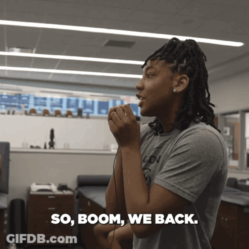 A Woman In A Grey Shirt Is Talking Into A Microphone With The Words So Boom We Back Written Below Her GIF