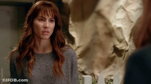A Woman In A Grey Sweater Is Looking At Another Woman In Front Of A Wall Of Crumpled Paper . GIF