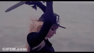 A Woman In A Hat Is Holding A Sword Over Her Head In The Air . GIF