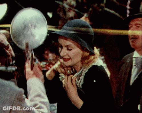 A Woman In A Hat Is Looking In A Mirror GIF