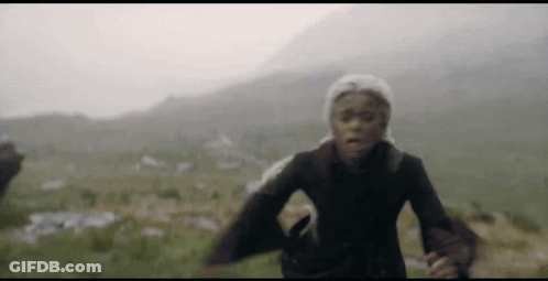 A Woman In A Hat Is Running In A Field With Mountains In The Background . GIF