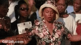 A Woman In A Hat Is Standing In A Crowd Of People . GIF