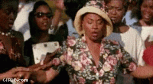 A Woman In A Hat Is Standing In Front Of A Crowd Of People Holding Hands . GIF