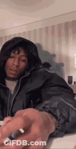 A Woman In A Hooded Jacket Is Sitting On A Bed And Holding A Marker . GIF