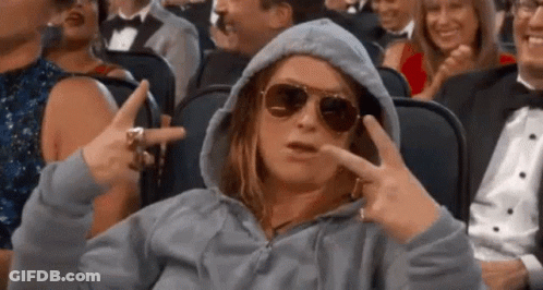 A Woman In A Hoodie And Sunglasses Is Sitting In A Crowd Of People In A Theater . GIF