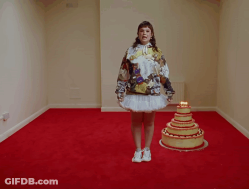 A Woman In A Hoodie Stands In Front Of A Cake With Candles On It GIF