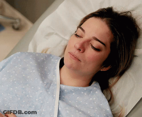 A Woman In A Hospital Gown Is Laying In A Bed With Her Eyes Closed GIF