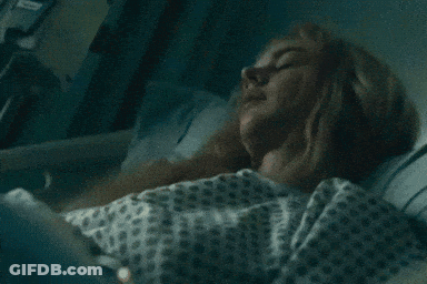 A Woman In A Hospital Gown Is Laying In A Hospital Bed With Her Eyes Closed . GIF