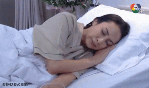 A Woman In A Hospital Gown Is Sleeping In A Hospital Bed GIF