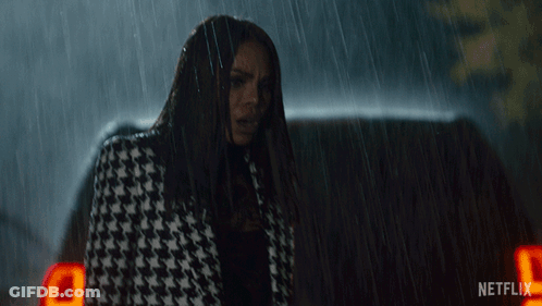 A Woman In A Houndstooth Coat Is Standing In The Rain Next To A Netflix Logo GIF