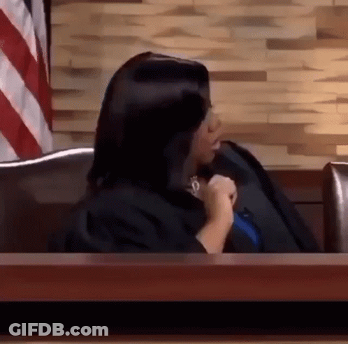 A Woman In A Judge 'S Robe Is Sitting At A Table In Front Of A Wooden Wall . GIF